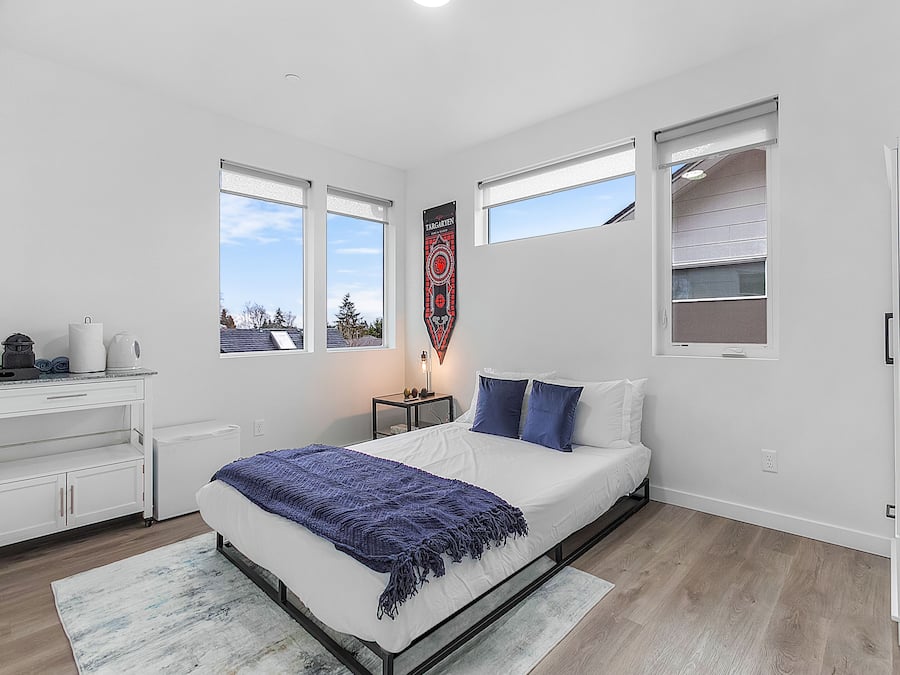 Quarto moderno com cama, mesa de cabeceira, cômoda e janela com vista.