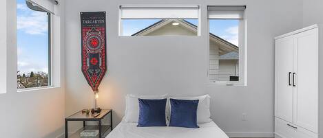 A bedroom with a bed, a nightstand, a wardrobe, and two windows.
