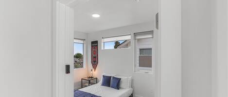 Une chambre moderne avec un lit, deux fenêtres, une table de chevet et un luminaire fixé au mur.