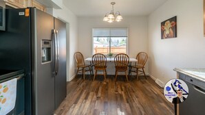 A kitchen with a stainless steel refrigerator, wooden chairs, a dining table, and a window with blinds. - Buffalo Jump Retreat - Extended Stay (Great Falls)