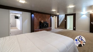 A bedroom with a large bed, a fireplace, and a staircase leading to another level. - Buffalo Jump Retreat - Extended Stay (Great Falls)