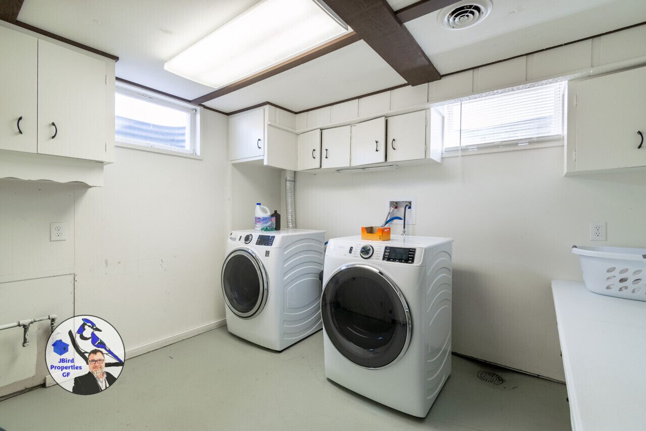 Une buanderie équipée de deux machines à laver à chargement frontal, d’un sèche-linge et d’un panier à linge blanc posé sur un plan de travail.
