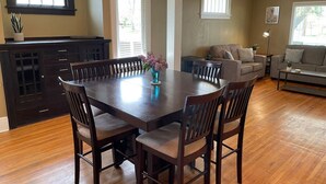 Un comedor con una mesa y sillas de madera, un florero con flores, y una zona de cocina con armarios y una ventana.