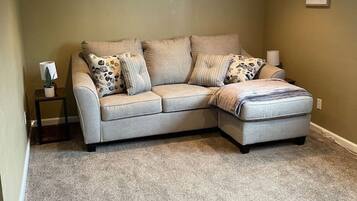 A corner living room with a beige sectional sofa, a small side table, and a carpeted floor.