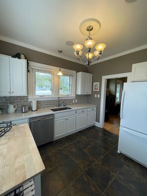 A kitchen with white cabinets, a dishwasher, a refrigerator, and a window. - Dragonfly House: A cheerful five-bedroom (Great Falls)