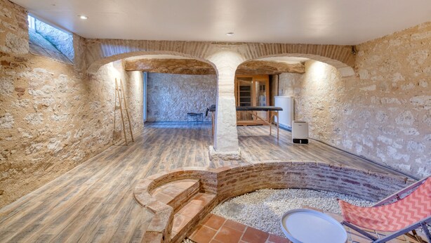 A rustic interior with exposed stone walls, a wooden floor, and a stone bench.
