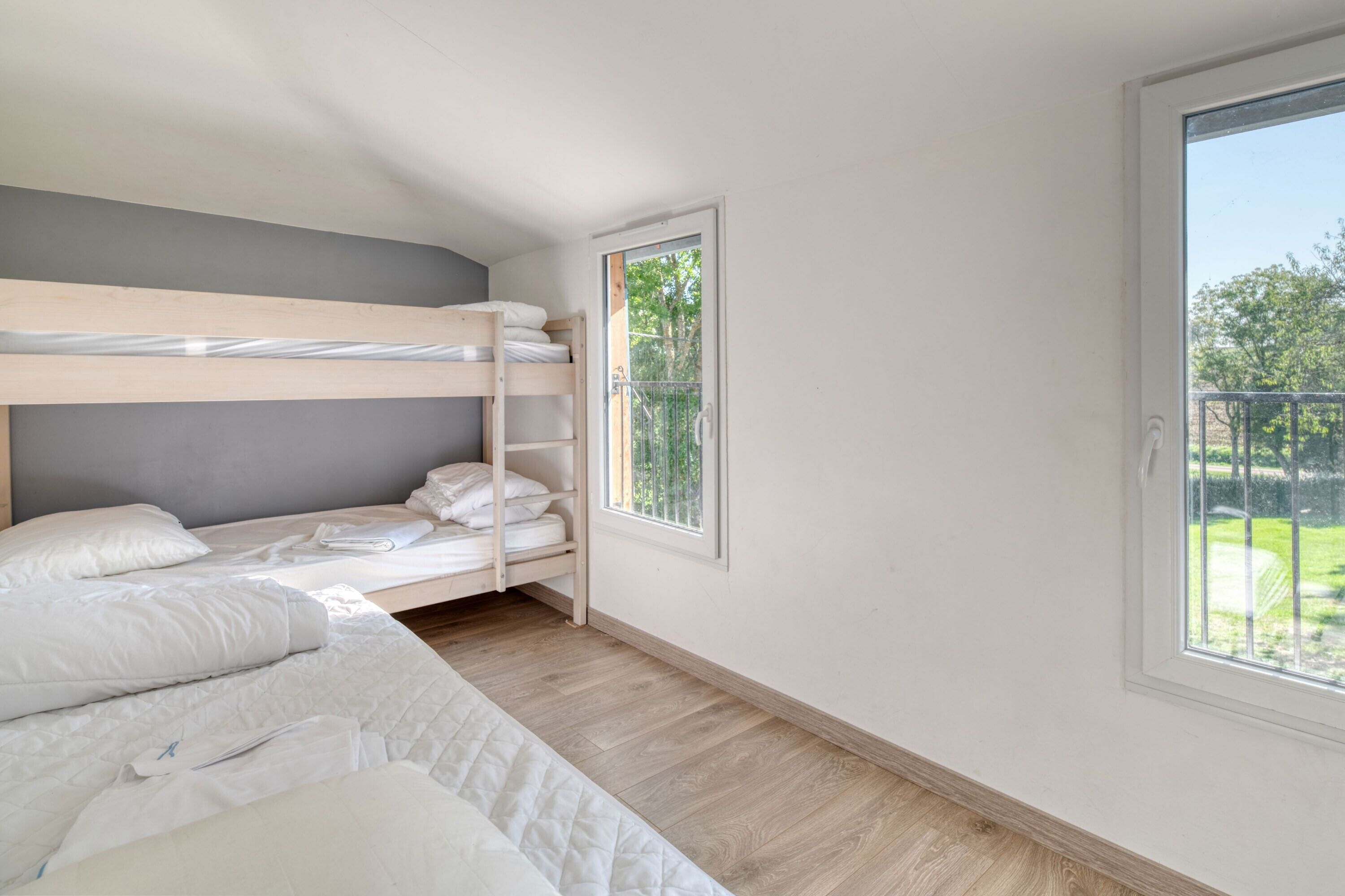 Een slaapkamer met stapelbedden, een raam met uitzicht op groen en een deur naar een buitenruimte.