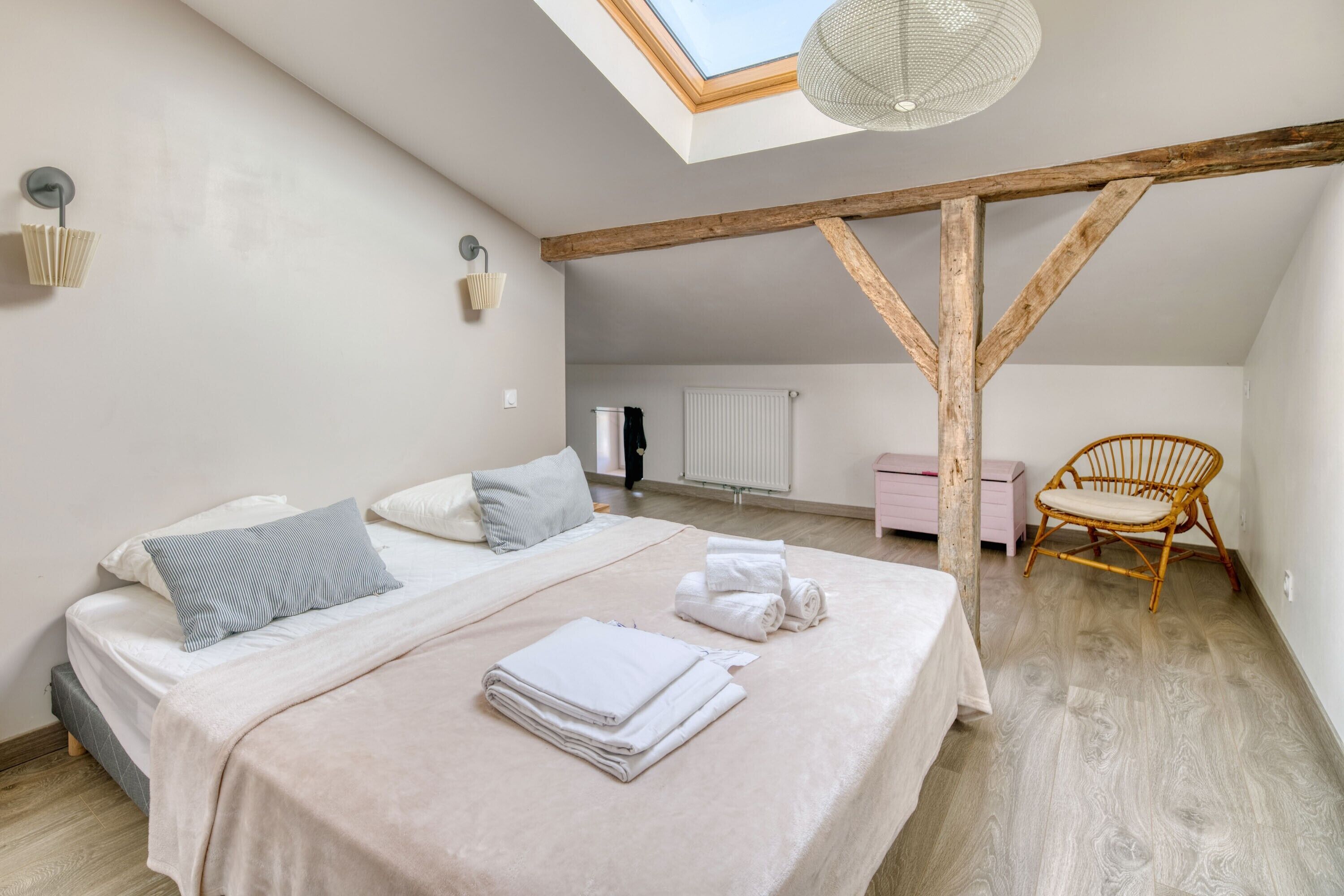 Een slaapkamer met een schuine kap, een bed met kussens, een stoel en een radiator.