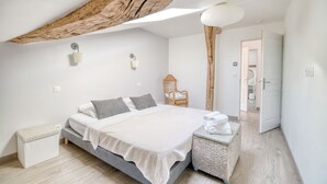 A bedroom with a bed, bedside tables, a chair, a hanging light fixture, and a door leading to another room.