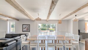 A modern dining area with a wooden table and white chairs, a black leather sofa, and a view of a garden through large windows.