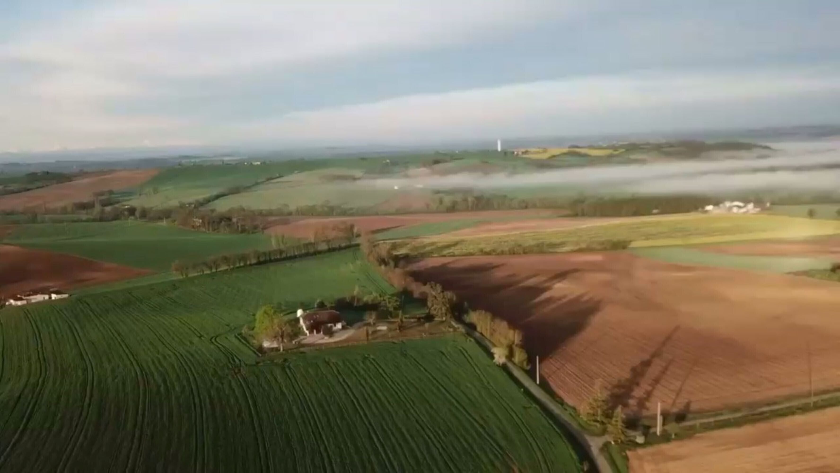 A rural landscape with fields, a small house, and a windmill.