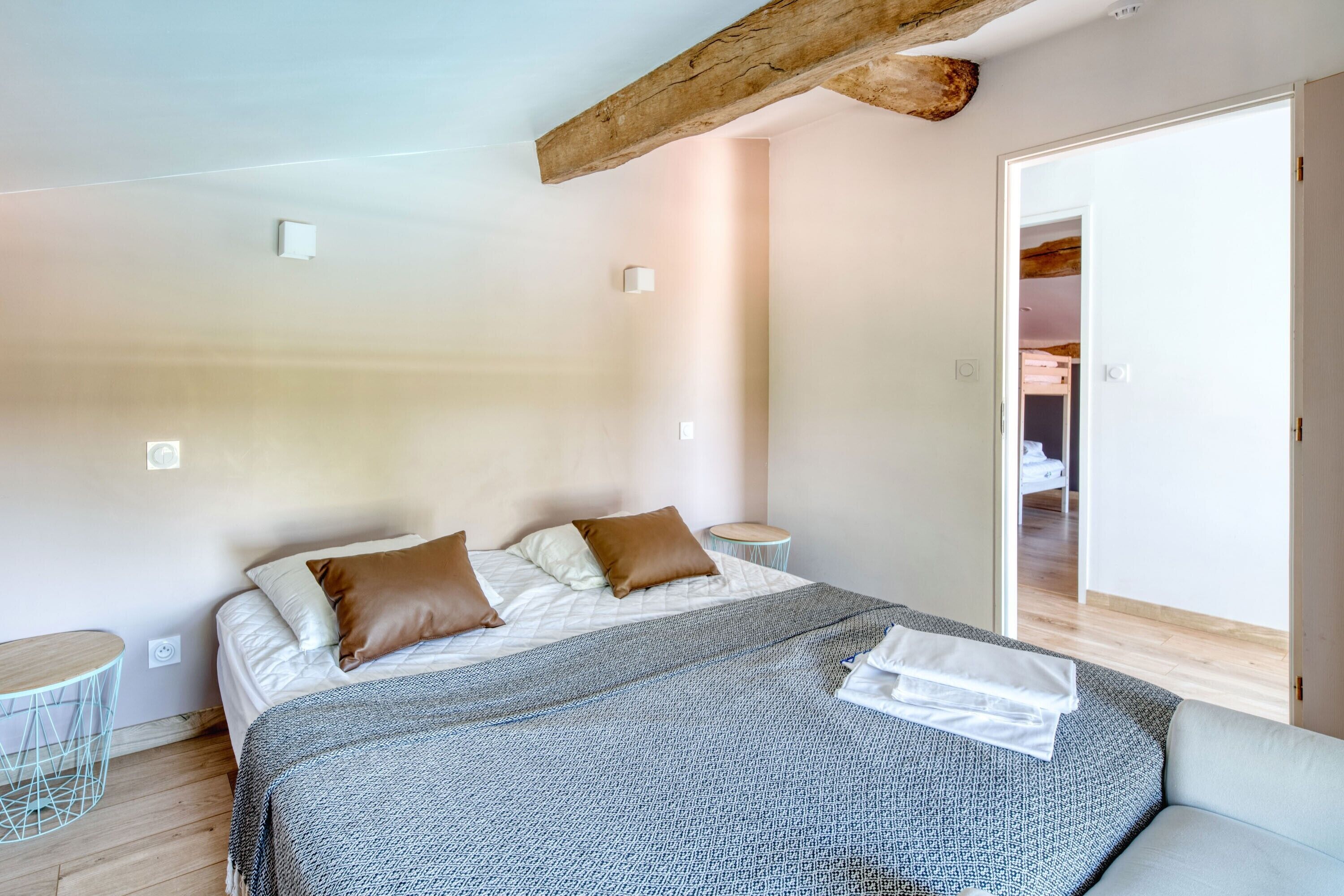 Un dormitorio con cama, almohadas, una mesita de noche y una puerta que da a otra habitación.