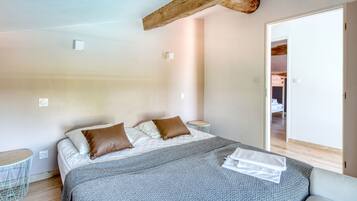 Un dormitorio con cama, almohadas, una mesita de noche y una puerta que da a otra habitación.