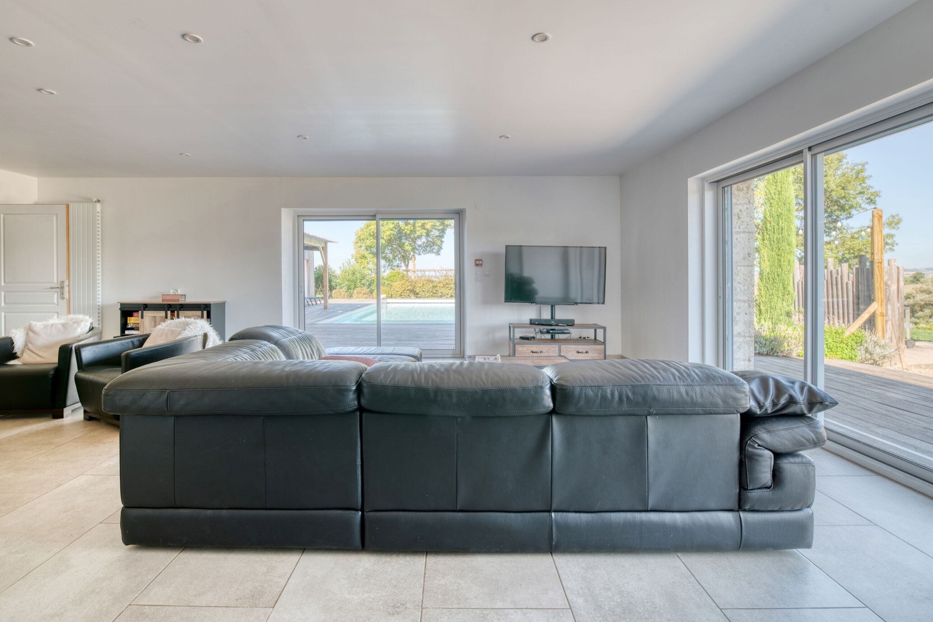 Ett modernt vardagsrum med en stor hörnsoffa, en platt-TV och en skjutdörr i glas som leder ut till ett utomhusområde.