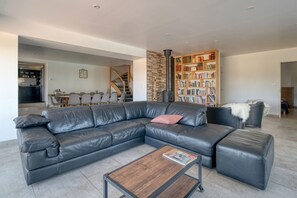 Una sala moderna con un sofá de cuero seccional, una mesa de centro, una chimenea, una estantería y un comedor al fondo.