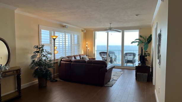 A living room with a brown leather sofa, a floor lamp, and a view of the ocean through large sliding glass doors. - Life is better at the beach!  Stunning, oceanfront, corner-unit condominium. (Daytona Beach Shores)