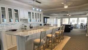 A modern kitchen with a central island, bar stools, and a dining area with a sofa and chairs. - Life is better at the beach!  Stunning, oceanfront, corner-unit condominium. (Daytona Beach Shores)