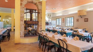 A dining area with multiple tables set for guests, featuring a stone archway and a vintage mechanical device. - HOTEL LE MACINE (Santa Cesarea Terme)