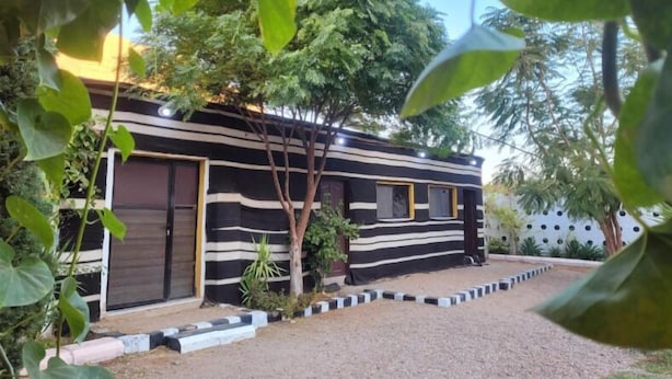 A modern, striped house with a gravel driveway, surrounded by greenery. - Wadi Rum Village Lodge (Wadi Rum)