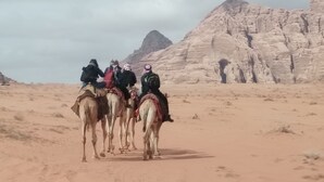 A group of people riding camels in a desert with rocky mountains in the background. - Wadi Rum Village Lodge (Wadi Rum)
