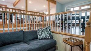 Een moderne woonkamer met een grijze bank, houten balustrade en een plafondventilator.