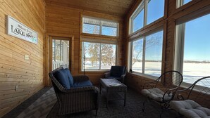 Een gezellig cabin interieur met houten wanden, een bord met de tekst 'Welcome to Our Lake House' en grote ramen met uitzicht op een besneeerd landschap.