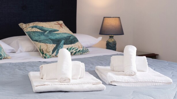 Un lit bien fait, avec des serviettes blanches, un coussin à motifs et une lampe sur une table de chevet.