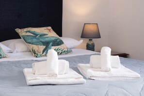 A neatly made bed with white towels, a patterned pillow, and a lamp on a bedside table. - Appartamento Noa 90 meters far from the beach (San Vito Lo Capo)
