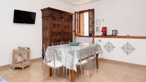 Un coin repas avec une table dressée pour quatre personnes, un téléviseur fixé au mur, un meuble en bois et une bouilloire rouge posée sur le comptoir.