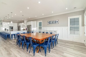 A spacious kitchen with white cabinets, a wooden dining table surrounded by blue chairs, and a sign that reads "BEACH".