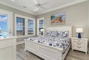 A bedroom with a large bed, a ceiling fan, a painting of a dog, and a window with blinds.