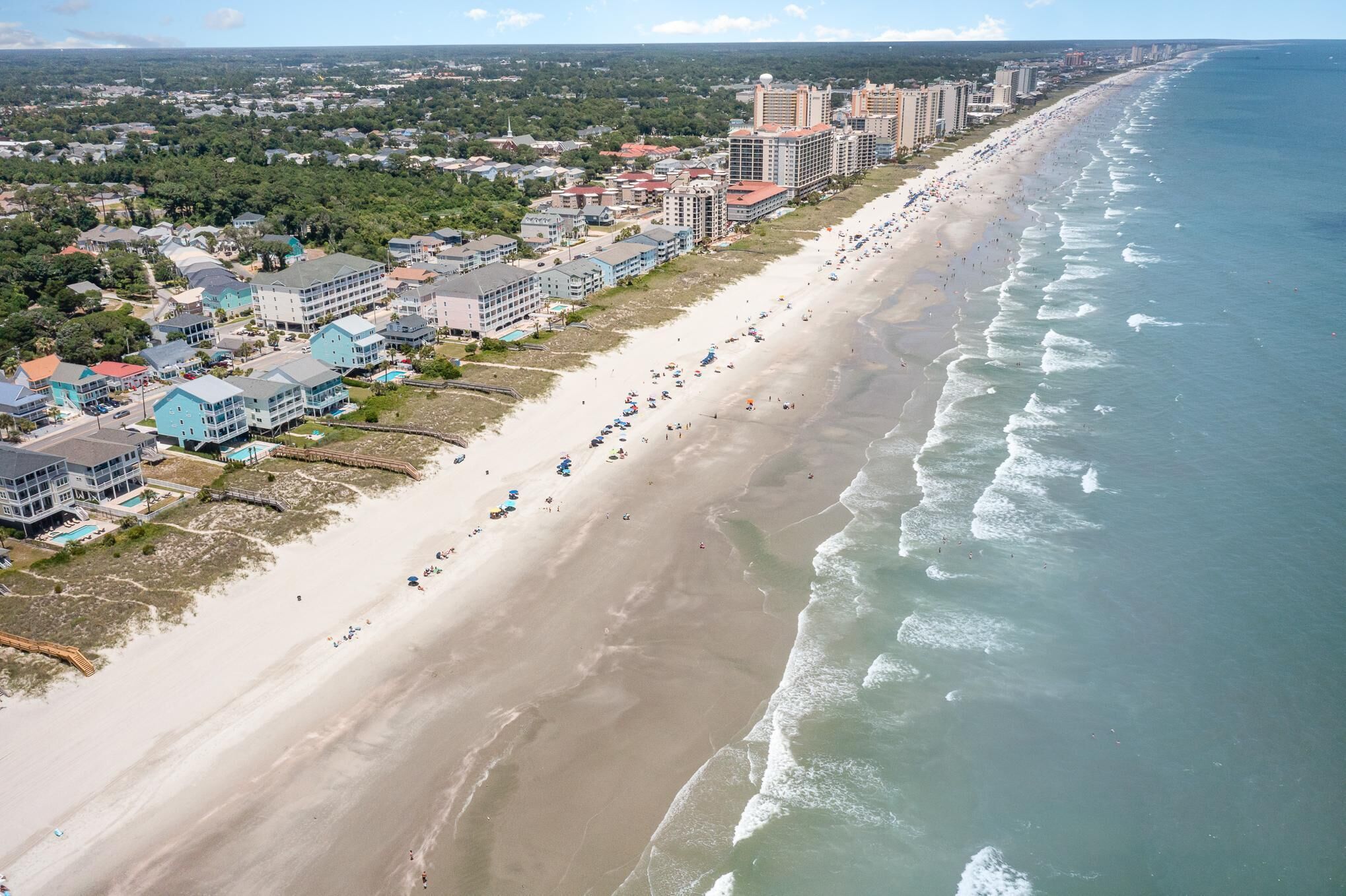Vista aerea di una zona costiera con una lunga spiaggia sabbiosa, edifici sul lungomare e una limpida visione dell'oceano.