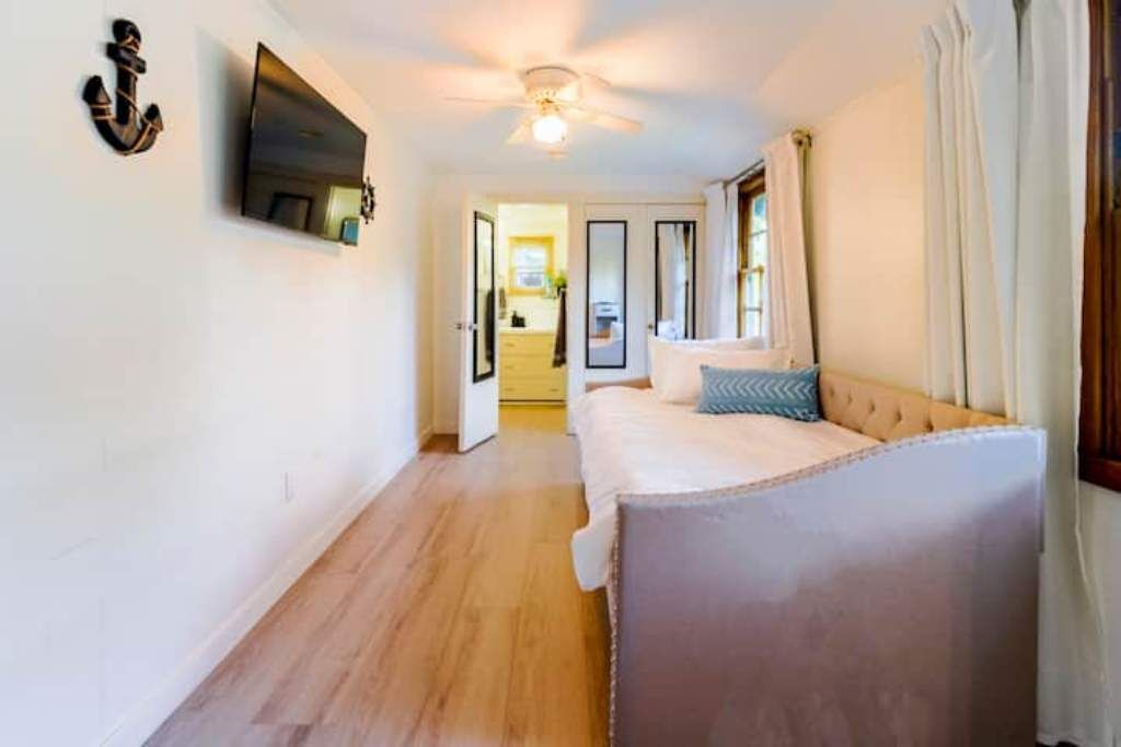 A bedroom with a bed, a ceiling fan, and a TV mounted on the wall.