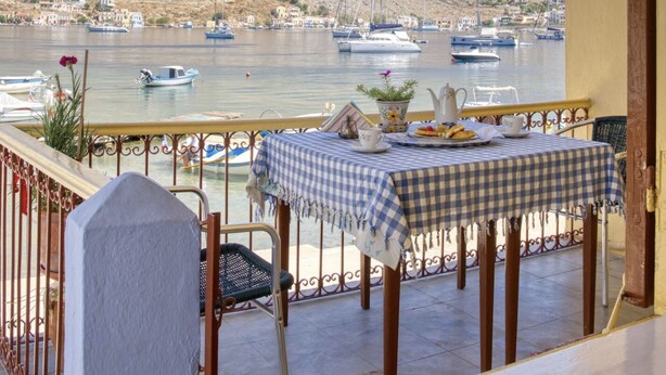 A balcony with a table set for two, overlooking a marina with boats and a mountainous backdrop. - 2islands Waterfront House (Symi)