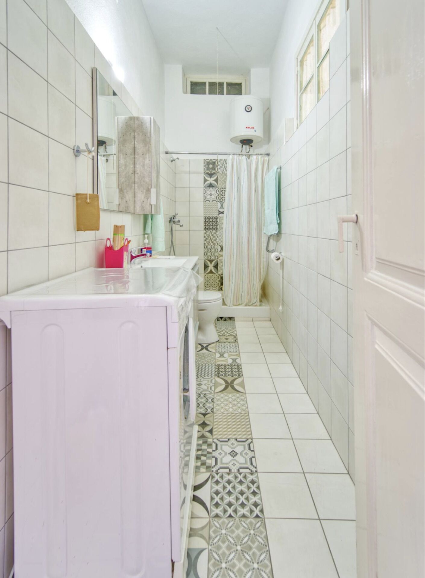 A narrow bathroom with a toilet, sink, and shower area.