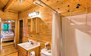 Interior de una cabaña de madera con baño que incluye lavamanos, espejo y cortina de ducha.