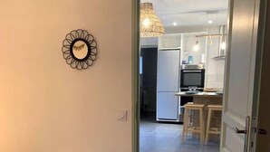 A hallway leading to a kitchen with a refrigerator, a dining area with a table and chairs, and a decorative wall piece.