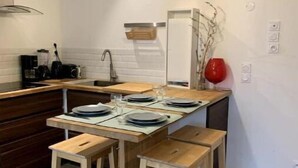 A modern kitchen with a wooden dining table and stools, a built-in oven, and a hanging light fixture.