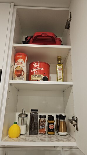 Een keukenkast met planken vol koffie, thee en kruiden.