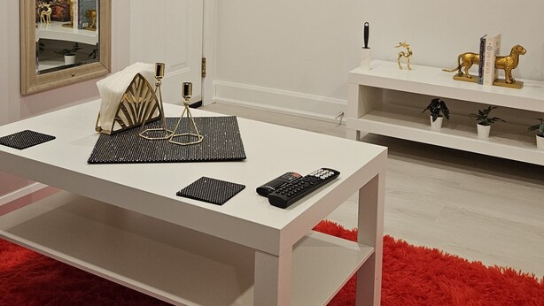 Una sala de estar moderna con una mesa blanca, alfombra roja y un televisor de pantalla plana montado en la pared.