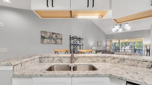 A kitchen with white cabinets, granite countertops, a double sink, and a dining area with a table and chairs.