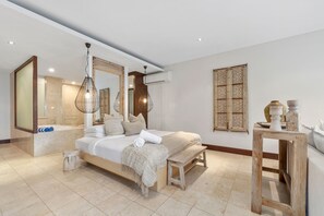 A modern bedroom with a large bed, a wooden bench, a small table, and a bathroom with a bathtub and a mirror. - Santai Resort (Casuarina)