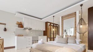 Un dormitorio moderno con una cama grande, un banco de madera y una cocina al fondo.