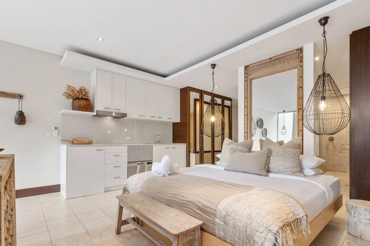 Una camera da letto moderna con un letto grande, una panca di legno e un angolo cottura sullo sfondo.