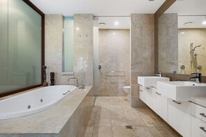 Een moderne badkamer met een ruime badkuip, twee wastafels en een douche.