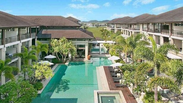 Un hotel con varios balcones, piscina central y abundante vegetación.