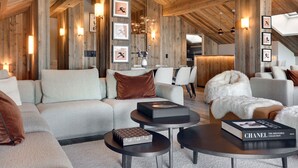 Um amplo loft com pé direito alto e vigas de madeira aparentes, apresentando uma sala de estar moderna com sofás, uma mesa de jantar e uma cozinha ao fundo.