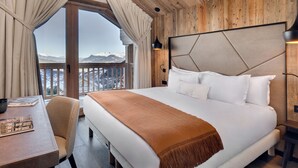 Quarto com cama grande, teto de madeira e vista para montanhas nevadas.