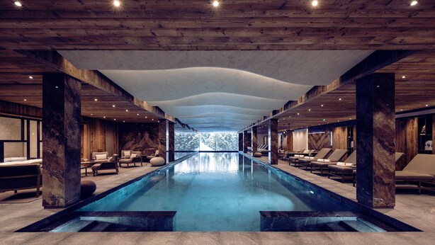 Piscina interior moderna com teto de madeira e colunas de mármore, rodeada por espreguiçadeiras e vista para árvores.