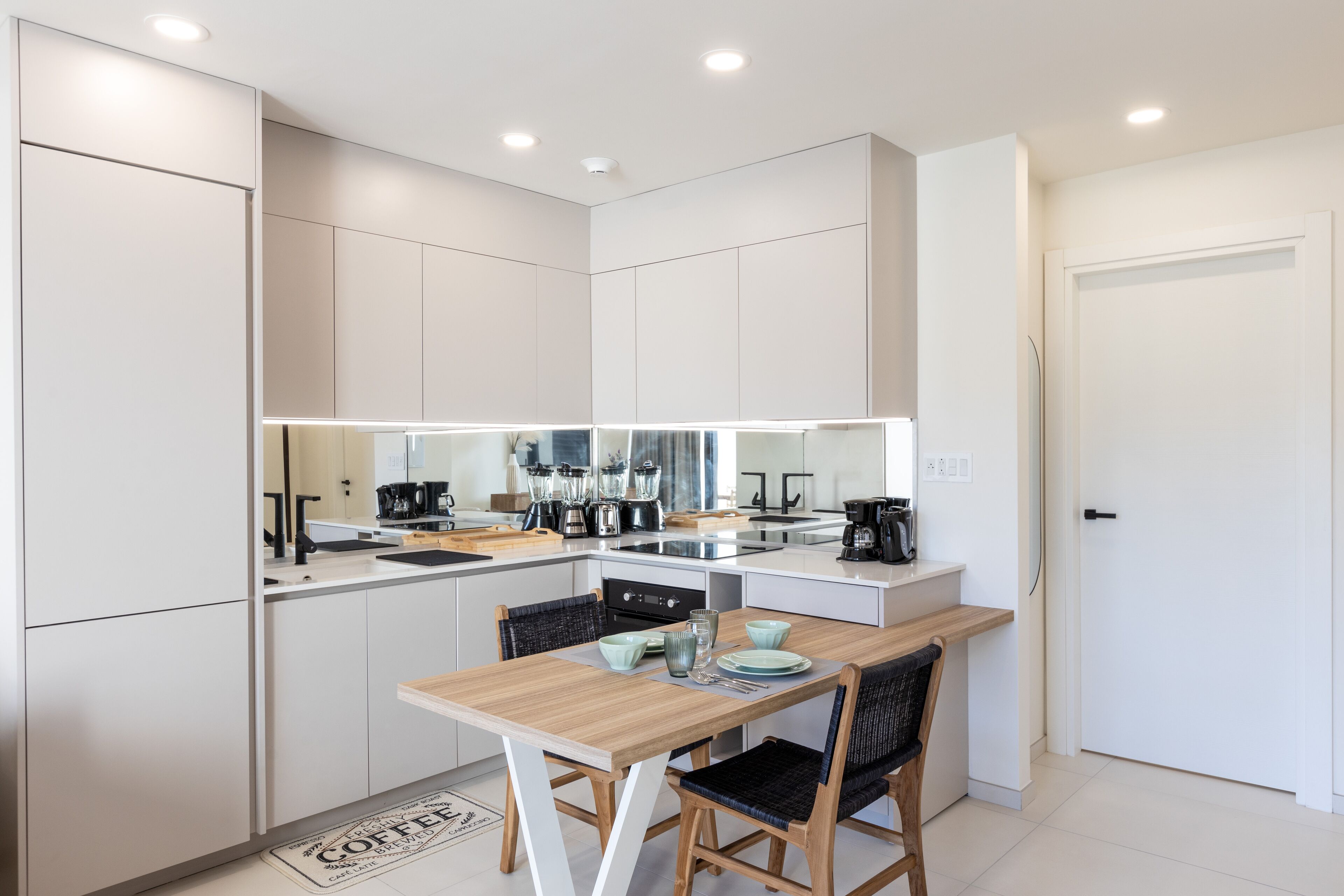 A modern kitchen with white cabinetry, a wooden dining table, and black chairs.